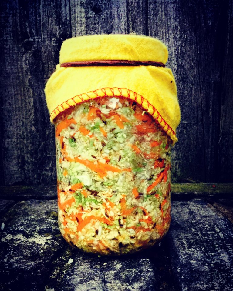 A jar of sauerkraut covered with a yellow cloth and a band