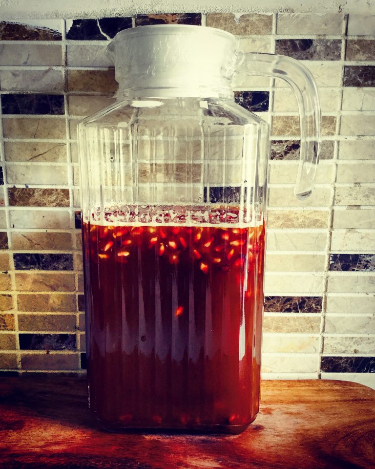 A jug of kombucha with pomegranate seeds floating on top