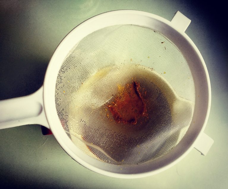 A sieve with fermented kombucha being strained into a jug
