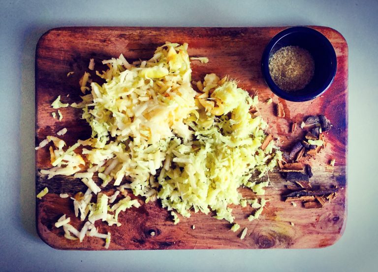 Grated apple, grated ginger, crushed cinnamon stick and sugar on a wooden board