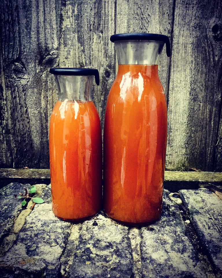 Two bottles of finished orange-brown kombucha on a stone wall