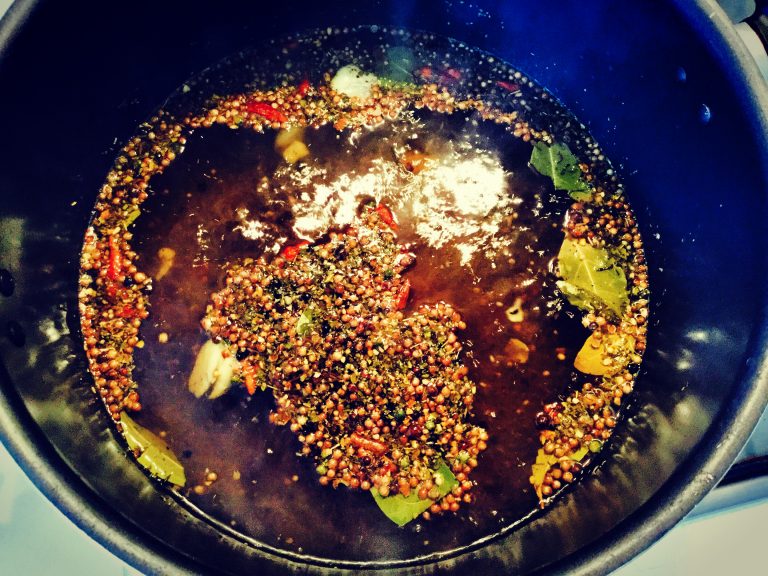 Vinegar brine with pickling spices, bay leaves and chili coming to the boil in a pan