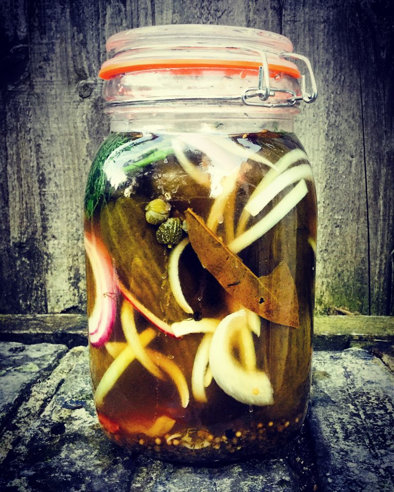 A clip-top jar of pickled gherkins with onions, dill, bay leaves and capers