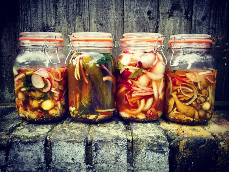 Four clip-top jars of different quick pickles lined up on a brick wall