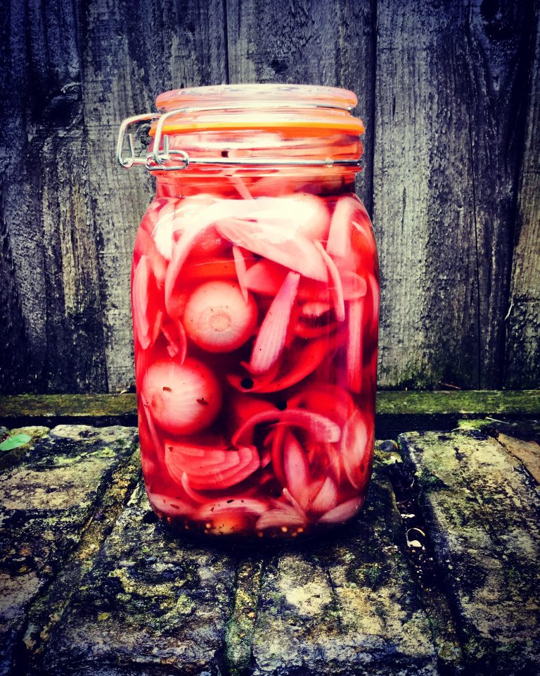 A clip-top jar of bright pink pickled red onions and pickling onions