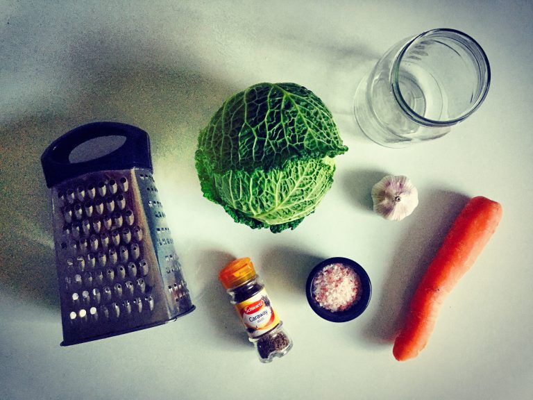 Ingredients for sauerkraut: a Savoy cabbage, carrot, garlic, salt, caraway seeds, a box grater and a glass jar