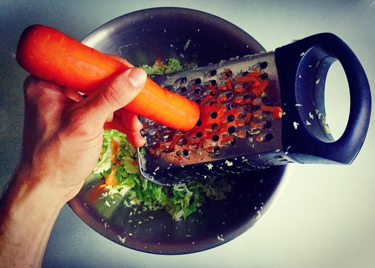 Grating a carrot into a bowl of grated cabbage
