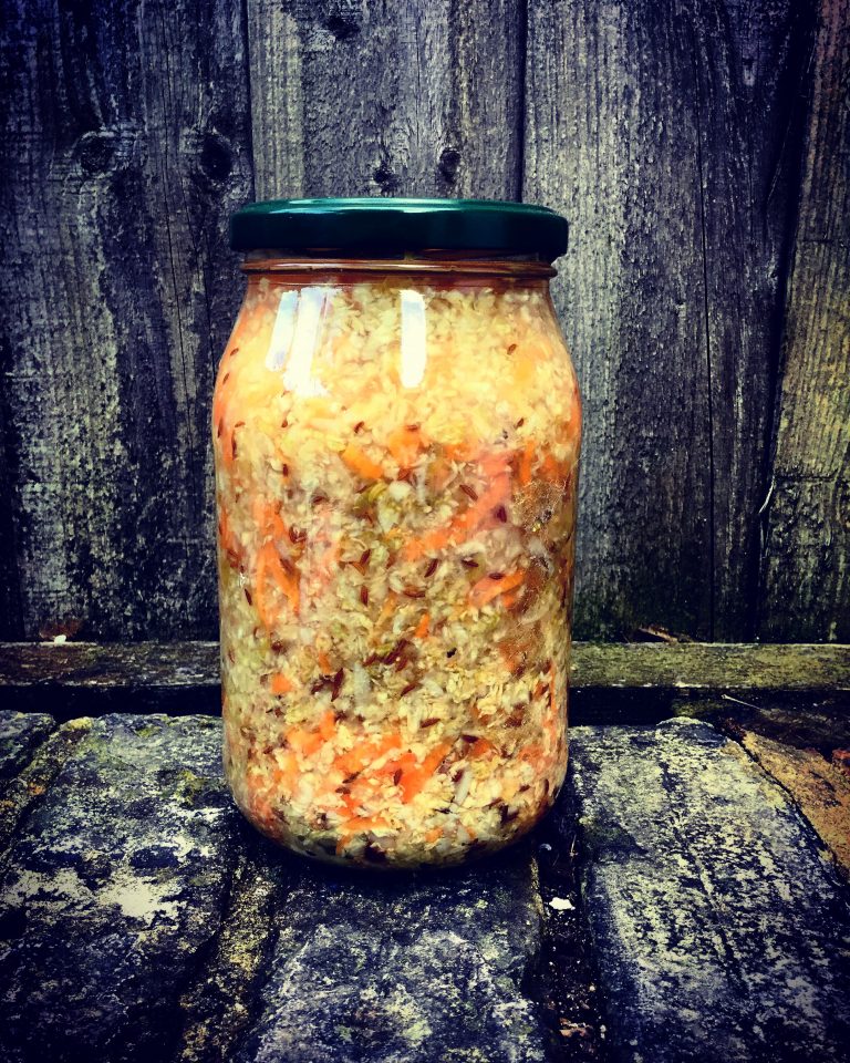 A lidded jar of finished sauerkraut with carrot and caraway