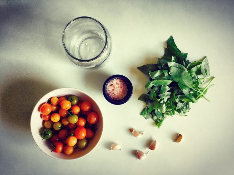 Ingredients for fermented cherry tomatoes: a bowl of mixed red, orange and yellow cherry tomatoes, fresh basil, garlic, salt and an empty jar
