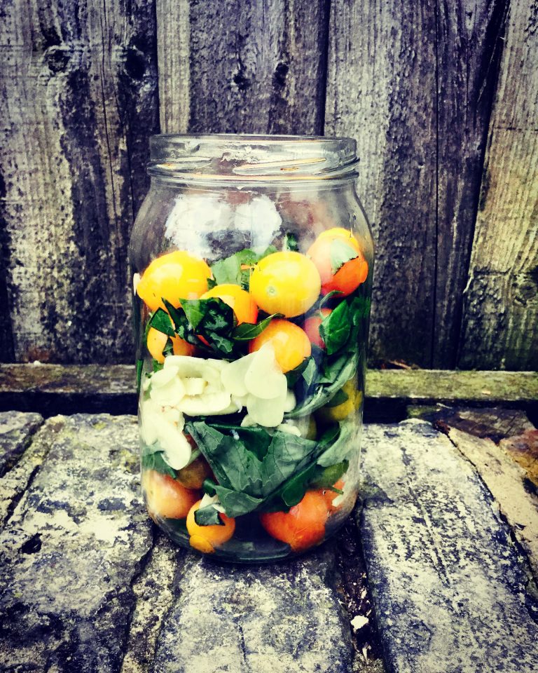 A jar layered with yellow and red cherry tomatoes, basil leaves and garlic slices