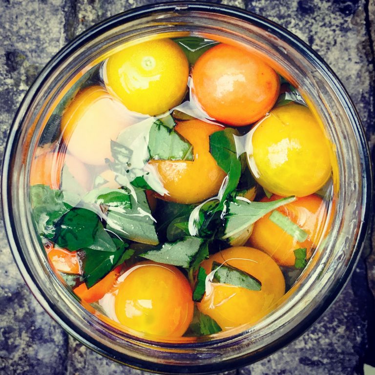Top view of cherry tomatoes and basil covered with brine in a jar
