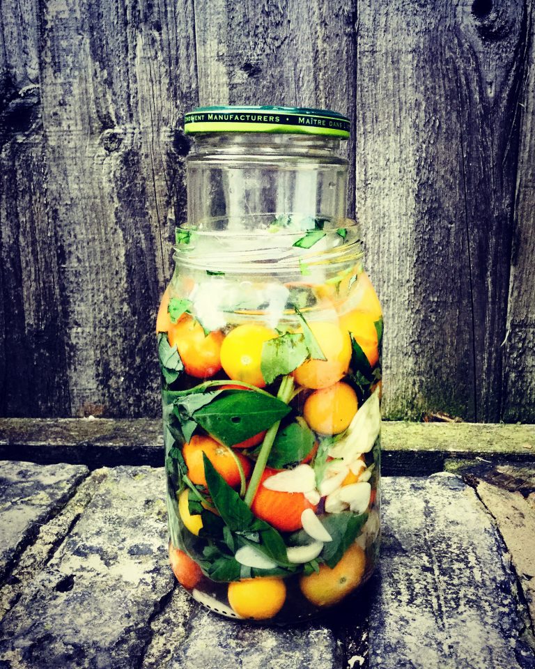 A small jar pressed into the neck of a larger jar of cherry tomatoes to keep them under the brine
