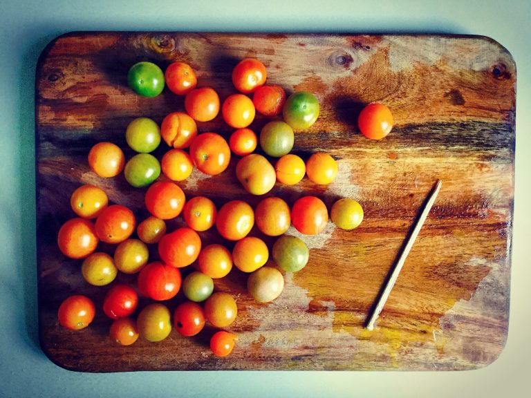 Mixed cherry tomatoes on a wooden board next to a toothpick