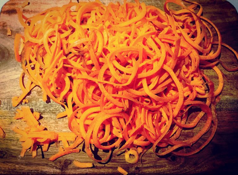 A pile of spiralized carrot noodles on a wooden board