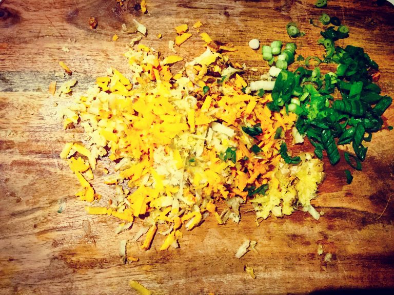 Grated ginger and turmeric next to sliced spring onions on a chopping board