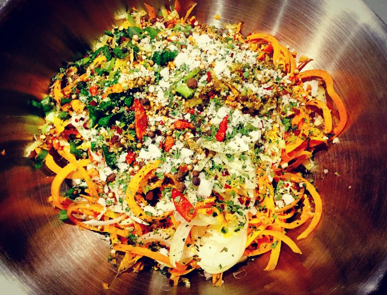 Spiralized carrots mixed with onion, chili, herbs, spices and salt in a steel bowl