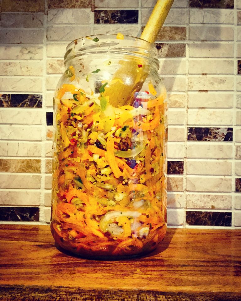 Spiced spiralized carrots packed into a large glass jar with a wooden spoon