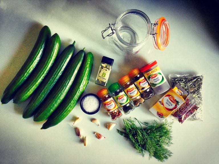 Ingredients for fermented pickles: long cucumbers, garlic, fresh dill, salt, jars of dried herbs and spices, and a clip-top jar