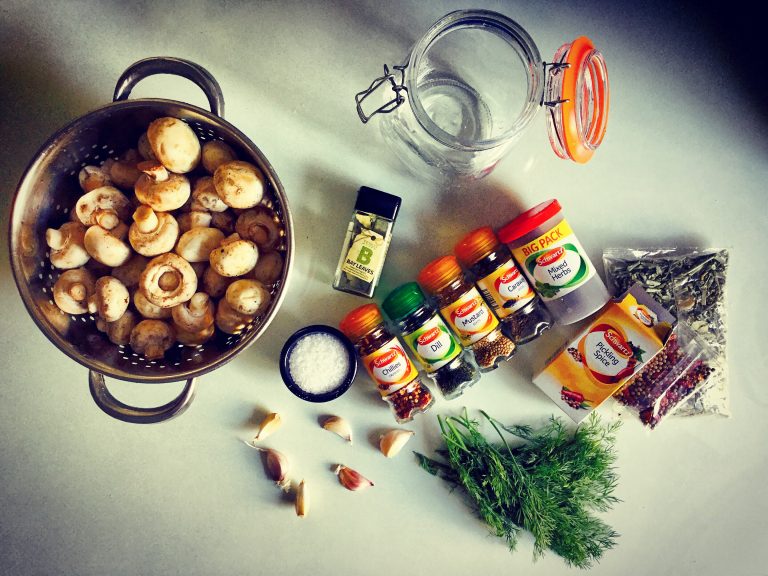 Ingredients for fermented mushrooms: a colander of button mushrooms, fresh dill, garlic, salt, jars of spices and a clip-top jar