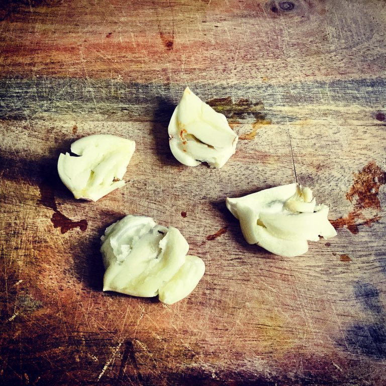 Four crushed garlic cloves on a wooden board