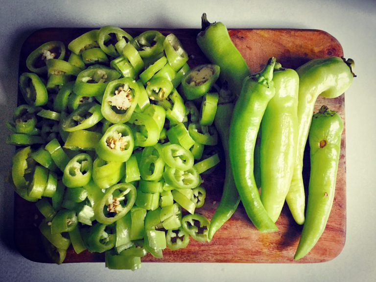 Banana peppers sliced into rings next to a few whole peppers on a wooden board
