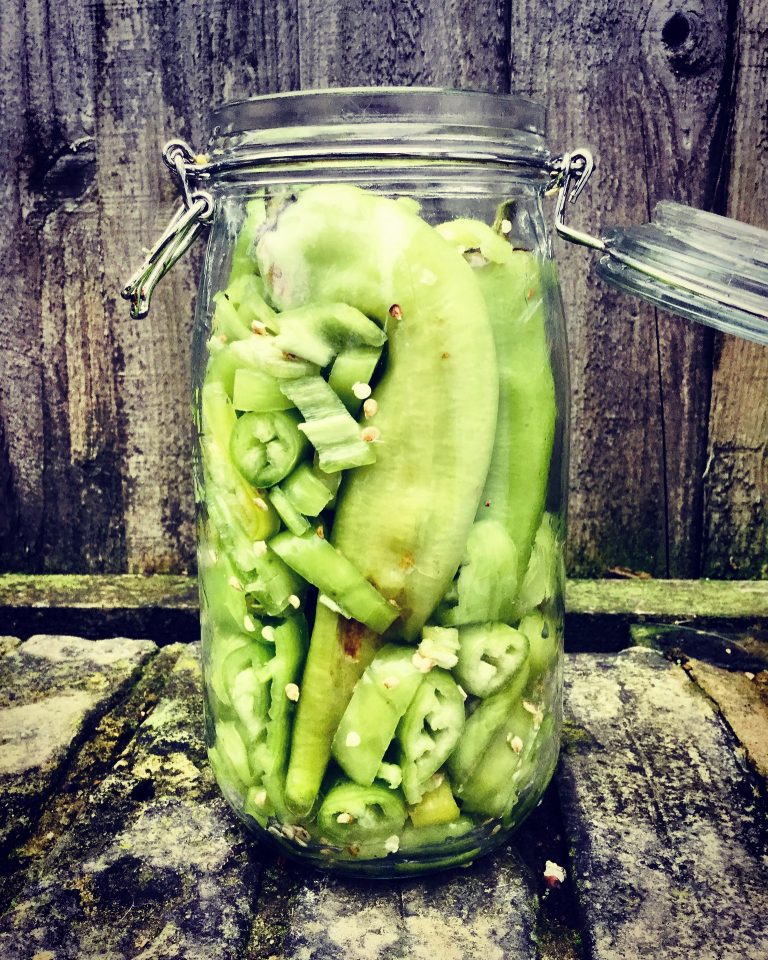 A clip-top jar packed with banana pepper rings and whole banana peppers