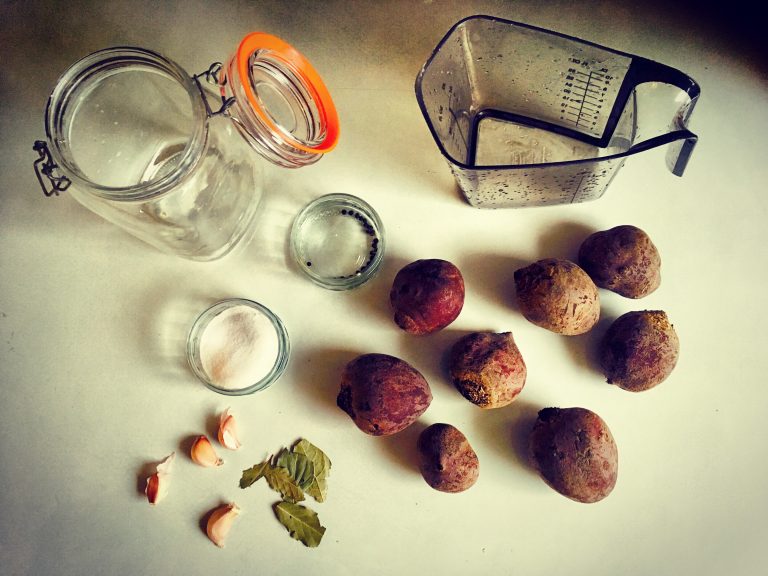 Ingredients for fermented beetroot: raw beets, garlic cloves, bay leaves, salt, peppercorns, a clip-top jar and a measuring jug