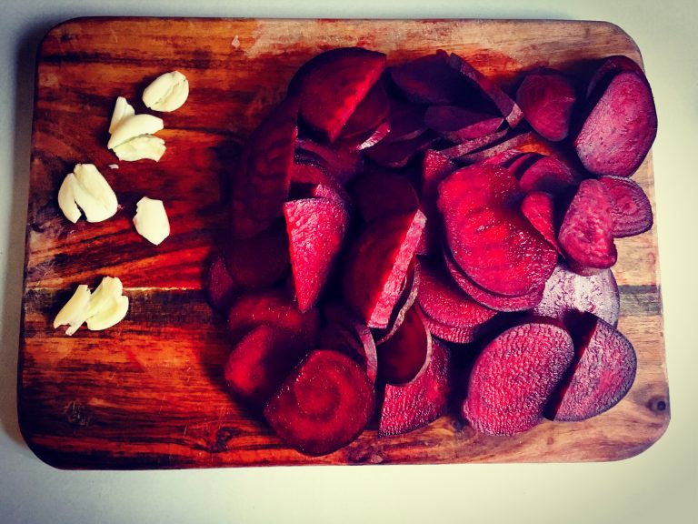 Thinly sliced raw beetroot and peeled garlic cloves on a wooden board