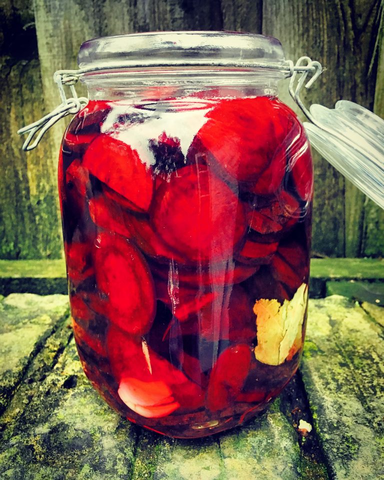 A clip-top jar of beet slices covered in deep red brine, with a bay leaf against the glass