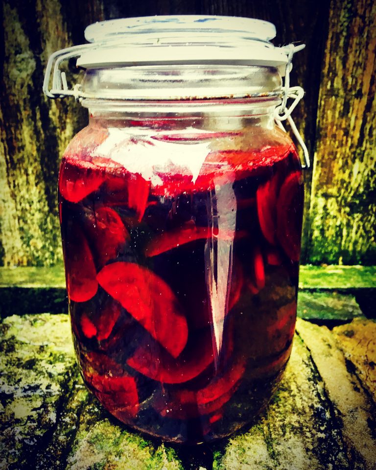A clip-top jar of finished fermented beetroot slices in dark red brine