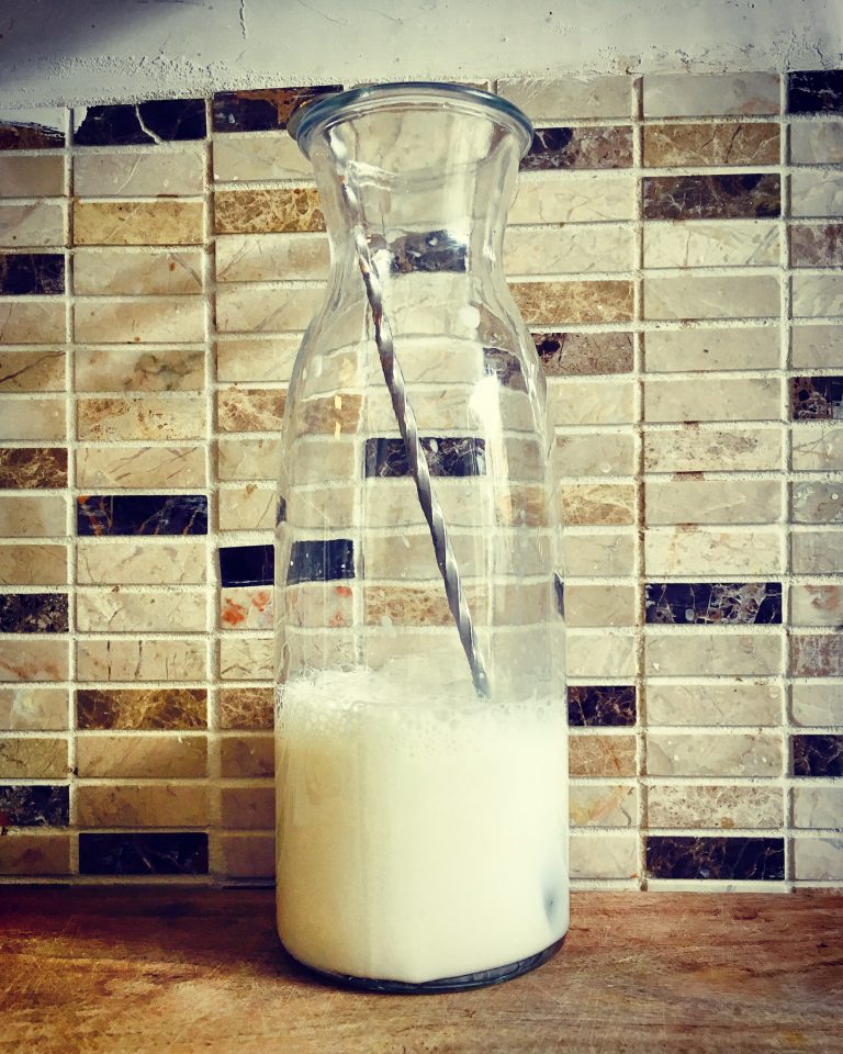 A glass bottle half full of milk with a long stirring spoon